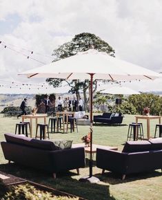 an outdoor seating area with tables and umbrellas on the grass, surrounded by trees