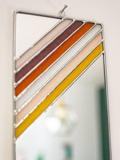 a mirror hanging on the side of a wall with multicolored strips in it