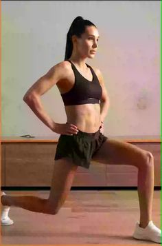 a woman in a black sports bra top and green shorts running on a wooden floor