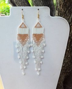 white and orange beaded fringe earrings on display next to tree with branches in the background