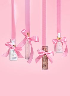 three bottles with pink ribbons hanging from them on a pink background next to each other