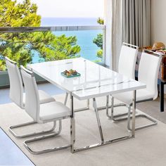 a dining room table with white chairs and an ocean view from the living room window