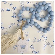 a tasseled necklace with blue beads and a white tag on it next to a flower wallpaper