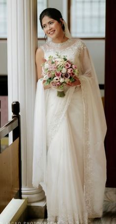 a woman in a white dress holding a bouquet and standing next to a pillar with columns