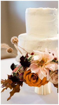 a wedding cake decorated with flowers and leaves on a white tableclothed table cloth