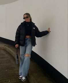 a woman in black jacket and jeans leaning against wall