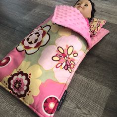 a doll laying on top of a pink and brown flowered sleeping bag with pillows