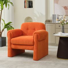 an orange chair sitting in a living room next to a table and potted plant