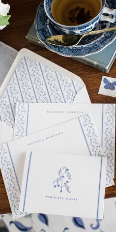 blue and white stationery on top of a wooden table next to a cup of tea