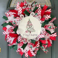 a christmas wreath with red and green bows on the front door, decorated with an ornament that reads merry christmas