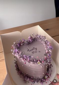 a heart shaped cake with purple flowers on it in a white box that says happy birthday