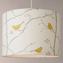 a white lamp shade with yellow birds on branches printed on the fabric, hanging from a ceiling fixture