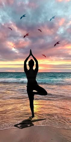 a person doing yoga on the beach with birds in the sky above them at sunset