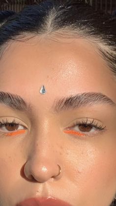 a woman with orange eyeliners on her nose and eyebrows is looking at the camera