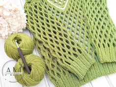 a green knitted sweater next to a ball of yarn and skeins of yarn