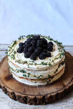 a cake with white frosting and blackberries on top sitting on a wooden board