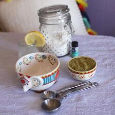 a table topped with bowls and measuring spoons next to a jar filled with powder