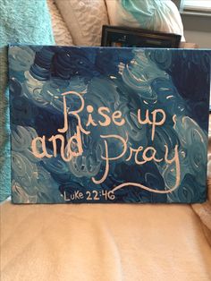 a painting with the words rise up and pray on it sitting on a couch next to a book