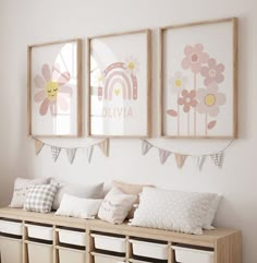 three framed pictures hang on the wall above a row of storage bins in a child's room