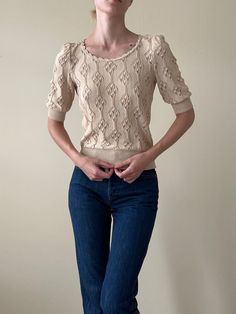 a woman standing in front of a white wall with her hands on her hips, wearing jeans and a sweater