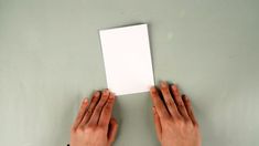 two hands holding up a white piece of paper against a gray background with copy space in the middle