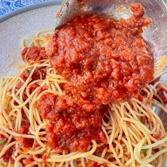 a plate full of spaghetti and sauce being stirred with a ladle on the side