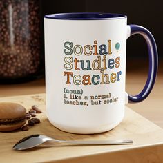 a white and blue coffee mug sitting on top of a wooden table next to a spoon