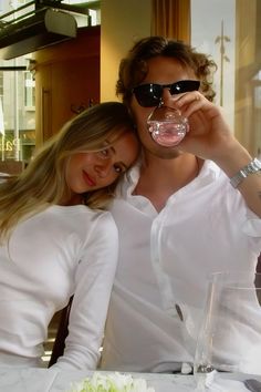 a man and woman sitting at a table drinking from wine glasses in front of them