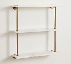 two white shelves with gold handles against a white wall, one shelf has marble and the other is brass