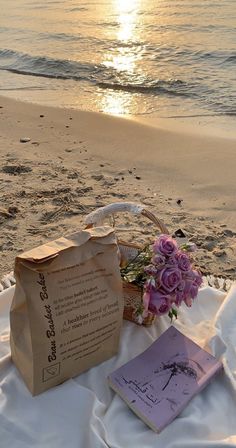 a basket with flowers and a book on a blanket at the beach