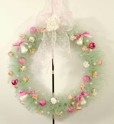 a green wreath with pink and white ornaments hanging from it's side on a wall