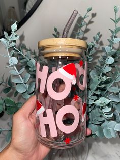 a hand holding a glass jar with the word ho hoo on it, surrounded by greenery