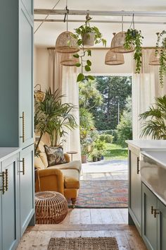 a living room filled with lots of plants next to an open kitchen door that leads to a covered patio