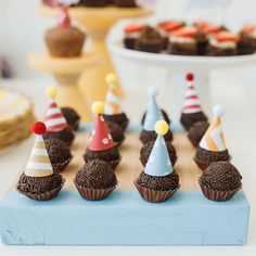 there are cupcakes with hats on them sitting on a blue tray in front of other desserts