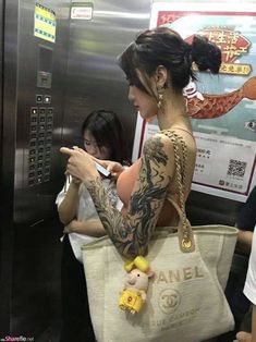 a woman with tattoos is looking at her cell phone while standing in front of an elevator