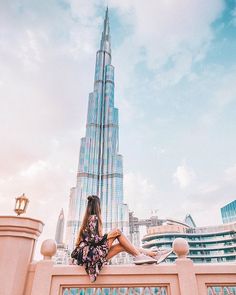 a woman sitting on top of a wall in front of a tall buliding