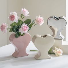 three ceramic vases with flowers in them on a table next to a heart shaped mirror