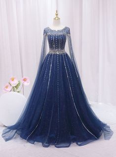 Aeonian elegance embodied in a dress, this blue gown is truly breathtaking! Capturing the essence of celestial beauty, it boasts an intricate overlay of sparkling sequins and delicate beading that illuminates the deep blue fabric beneath. The gown's fitted bodice highlights a sophisticated silhouette, cinched at the waist with a band of embellishments that enhance its figure-flattering design. Long, sheer sleeves and a gently scooped neckline add a touch of royal grace, perfect for a prom queen. The expansive skirt, speckled with glimmers like distant stars, flows into a soft, sweeping hem, making every movement a statement of grace and poise. This dress is designed for those who dream of a magical evening, wrapped in glamour and inspired by the night sky. Dark Blue Fantasy Gown, Starfall Ball Gown, Royal Blue Gowns Elegant, Royal Blue And Gold Dress, Blue Fantasy Dress, Blue Medieval Dress, Soft Blue Dress, Midnight Blue Gown, Navy Blue Evening Gown