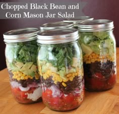 four mason jars filled with chopped black bean and corn mason jar salad on top of a wooden table