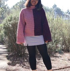 a woman standing in front of some bushes wearing a pink sweater and black leggings