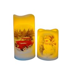 two lit candles with an image of a snowman and a red truck on them