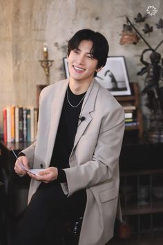 a young man sitting on top of a chair in front of a book shelf holding a piece of paper