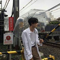 a man holding an umbrella while standing next to train tracks