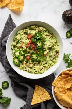 a white bowl filled with guacamole surrounded by tortilla chips and jalapenos