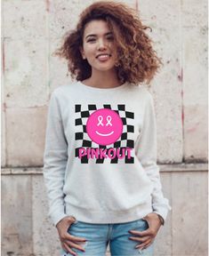 a woman with curly hair standing in front of a wall wearing a pink and black sweatshirt