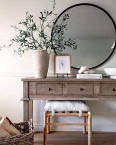 a wooden table topped with a mirror and a vase filled with green plants next to a stool