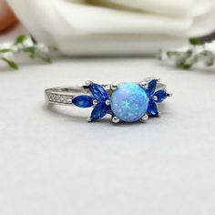 This beautiful ring is made from genuine 925 sterling silver with rhodium plating. Ring details- -The Main stone is a round cut 6mm Lab Created Light Blue Opal Stone -Side stones are 4mm by 2mm Lab Blue Sapphire Marquise and 1mm Round simulated diamonds -Ring is casted in solid 925 sterling silver with rhodium plating (yellow gold and rose gold plated also available, please check the drop down menu for more options) -The Total face height of the ring measures 7mms and the band width measures 1.5 Blue Cubic Zirconia Promise Jewelry, Turquoise Sapphire Jewelry For Anniversary, Blue Cubic Zirconia Round Band Jewelry, Blue Opal Birthstone Ring In Sterling Silver, Blue Cubic Zirconia Birthstone Ring For Promise, Blue Cubic Zirconia Birthstone Promise Ring, Blue Cluster Ring With Center Stone, Round Cut, Blue Round Jewelry For Promise, Blue Cubic Zirconia Crystal Ring