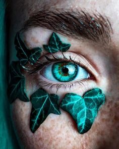 a person with green leaves painted on their face and blue eyes is looking at the camera