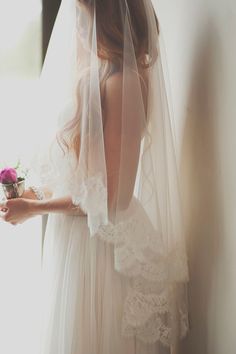 the back of a woman's wedding dress, with her veil pulled up and flowers in her hand