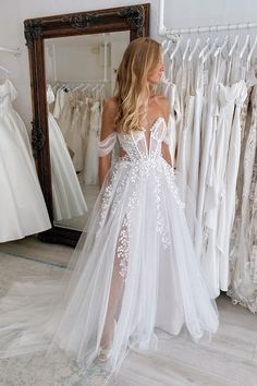 a woman standing in front of a mirror wearing a white wedding dress with flowers on it